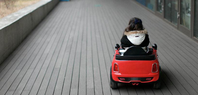Ein kleines Mädchen sitzt in einem Spielzeug-Auto. Kinderautositze sind Pflicht.