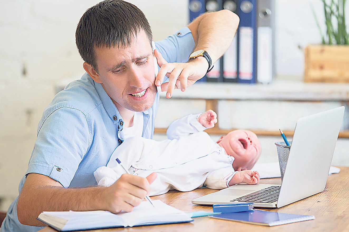 Ein gestresster Vater mit Säugling im Büro. Thema: Vaterrolle im Wandel