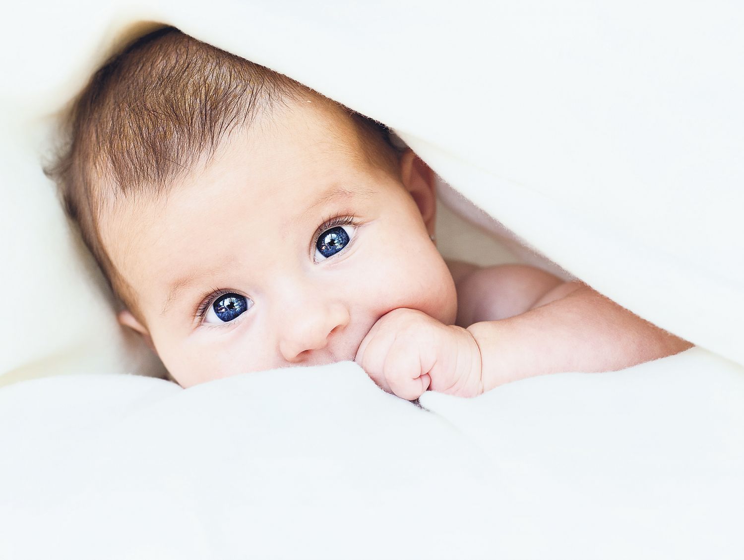 Ein Baby schaut unter einer Decke hervor. Thema: Kinder bekommen