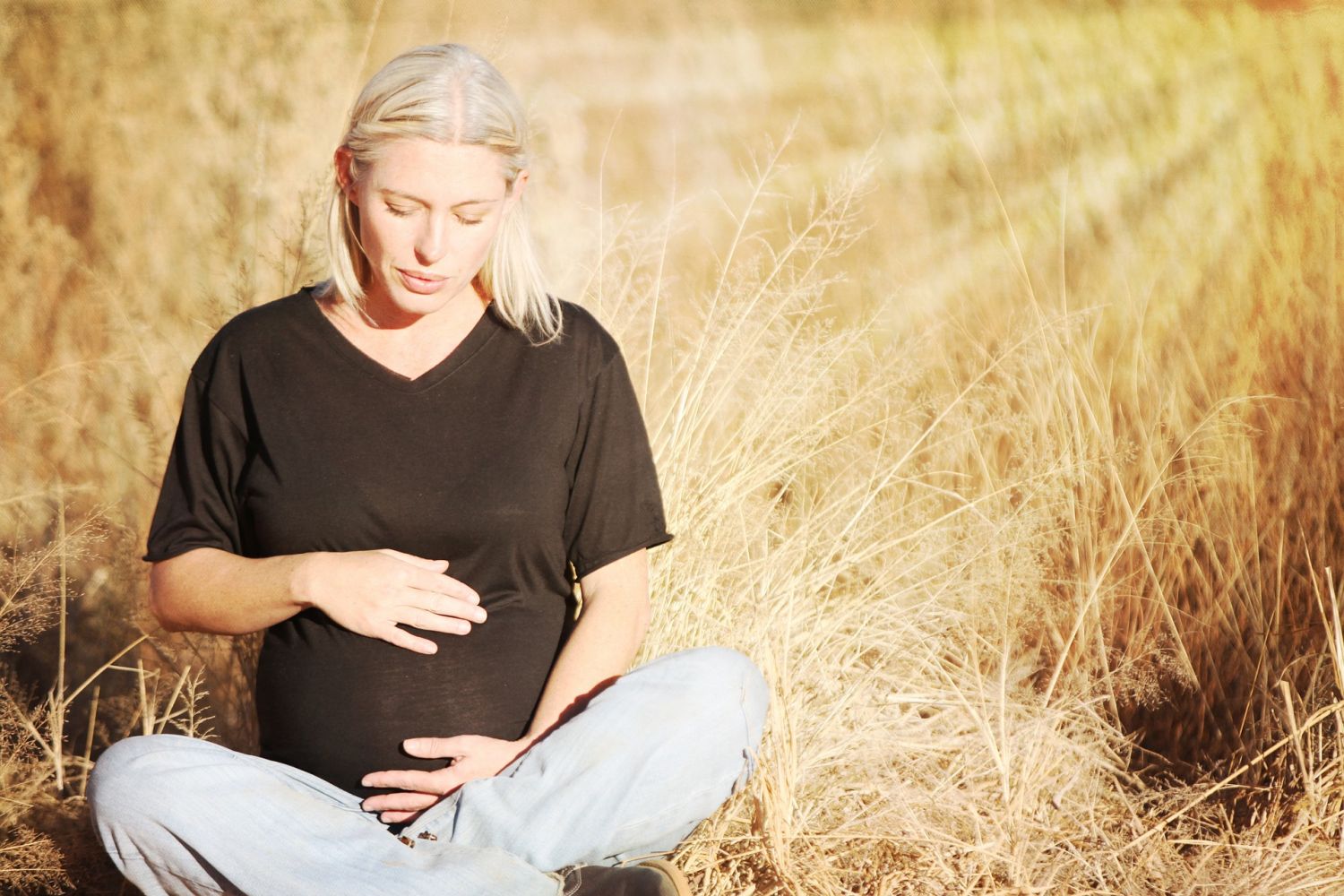 Schwangere Frau sitzt in der Sonne und streichelt ihren Bauch. Thema: PND